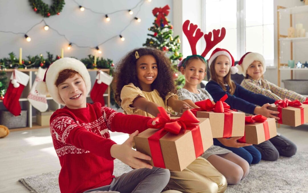 Group of smiling children in Santa hats and reindeer antlers sitting in row holding presents, willing to share joy, kindness and holiday spirit and wishing everyone Merry Christmas and Happy New Year