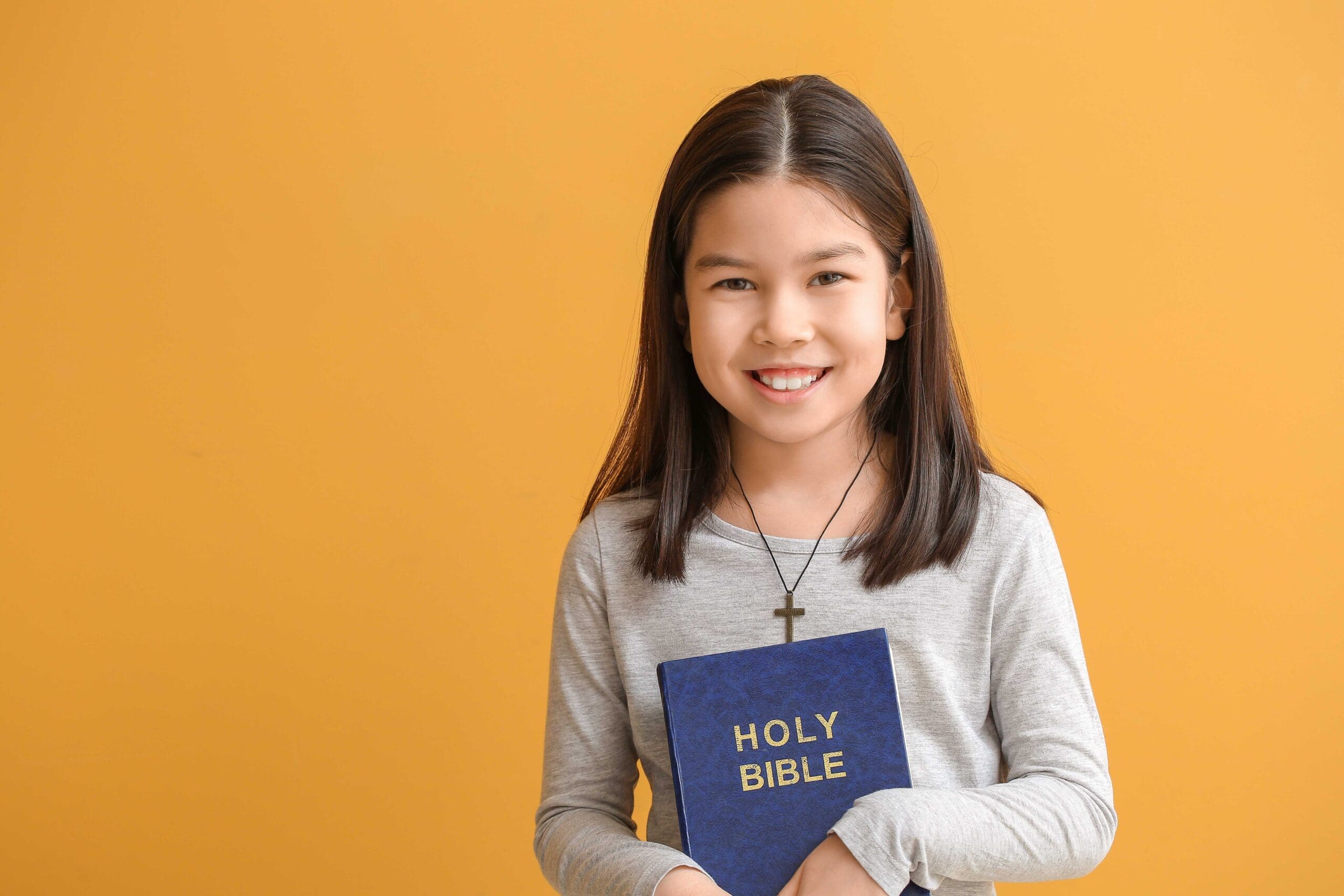 Asian girl with Bible on yellow background