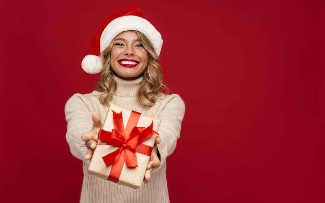 girl in Santa Claus hat showing gift box isolated over red background