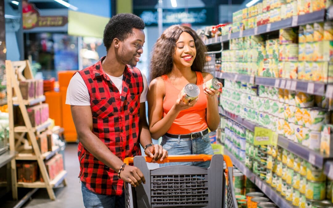 smiling african american man and woman with shopping cart choosing canned goods in supermarket