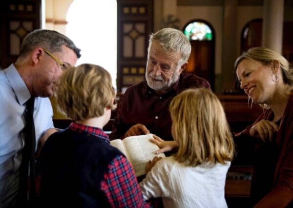 A man at church showing two children a part of the Bible with two adults beside him.