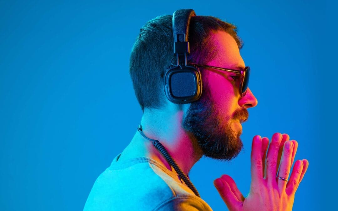 Young man wearing sunshades and headphones with a blue background with his hands up in prayer position.