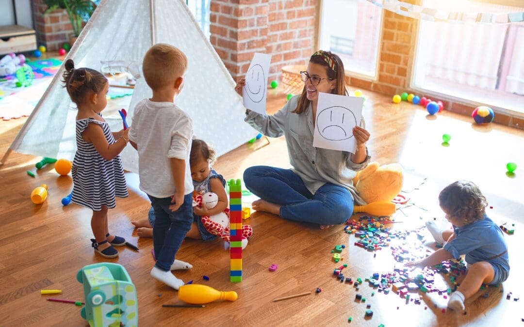 Teacher playing with several children. Building blocks and a tent are on the floor.